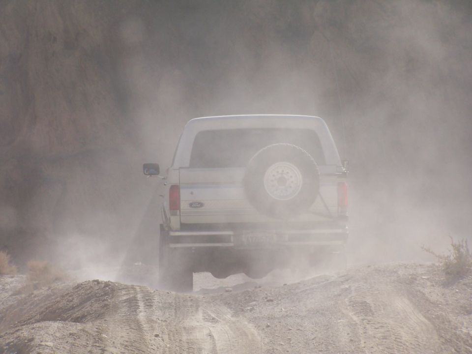 White Ford pickup or SUV kicking up dust on a dirt road