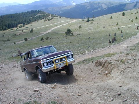 1979 Ford Bronco - A 1978 Ford Bronco navigates a steep, dusty mountain trail with a scenic backdrop of hills and sky.