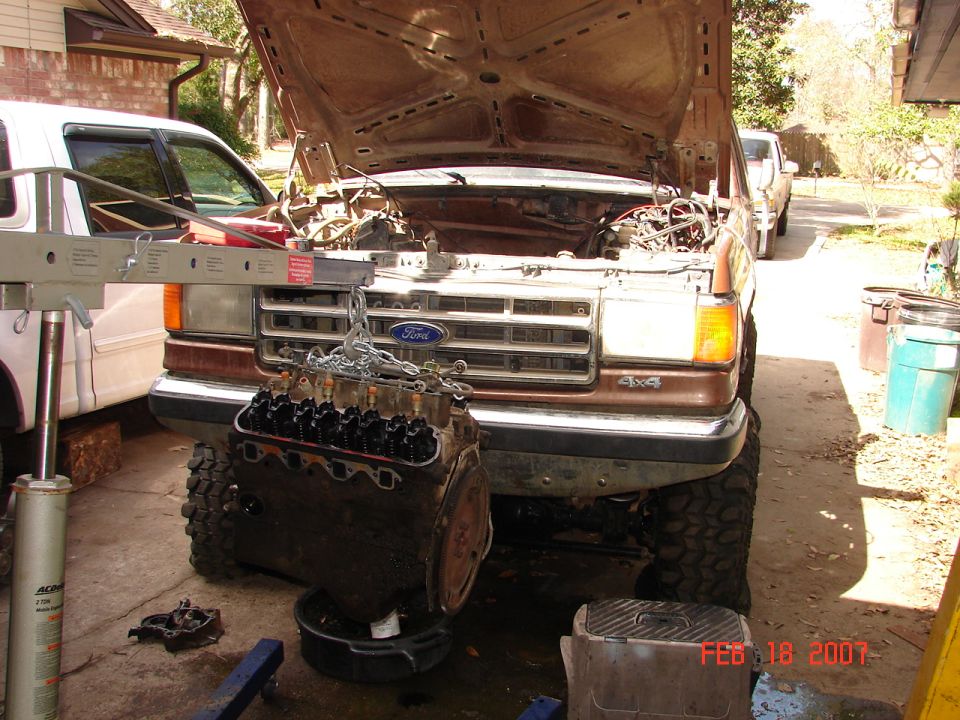 Brown Ford truck with hood open, engine being removed by hoist. Visible "4x4" badge