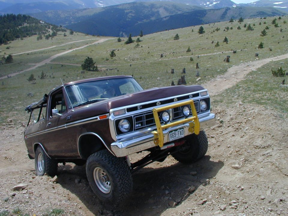 Brown topless Ford Bronco with yellow brush guard on a mountain dirt trail