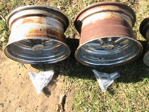 1973 Ford Ranchero - Two rusty aluminum wheels and two hubcaps are displayed on the ground.