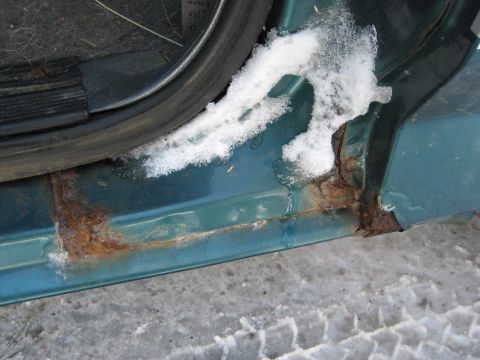 1994 Ford Bronco - Close-up of a vehicle's rusted door sill with snow and melting ice.