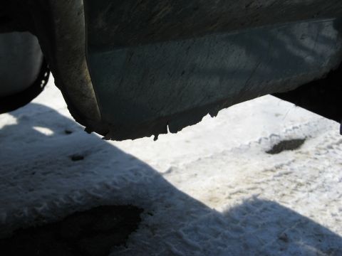 1994 Ford Bronco - The lower body panel of a vehicle shows significant rust and damage, with a snowy surface below.