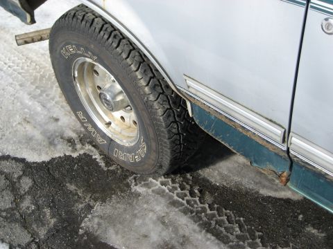 1994 Ford Bronco - The side of a 1994 Ford Bronco is shown with a tire on a wet, snowy surface, revealing some rust on the lower body panel.