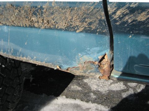 1994 Ford Bronco - Close-up of a teal vehicle's lower body panel showing extensive rust damage and dirt accumulation.