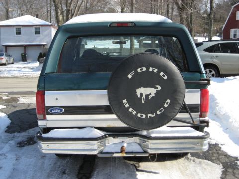 1994 Ford Bronco - The rear of a green Ford Bronco is shown with a spare tire cover and a snow-covered landscape.