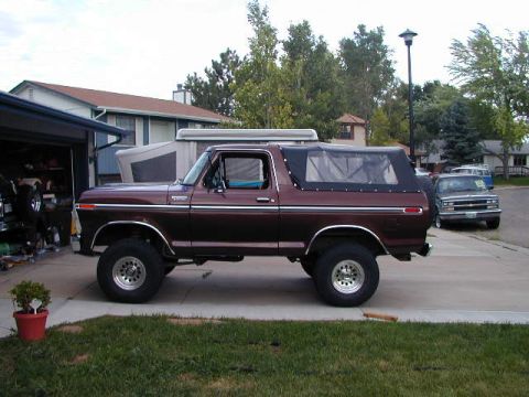 1979 Ford Bronco - Passenger-side profile of a maroon full-size Ford Bronco with a black soft top and clear side windows, parked on a residential driveway wit…