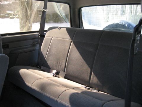 1994 Ford Bronco - Rear interior view of a 1994 Ford Bronco, showing the bench seat and a spare tire mounted behind it.