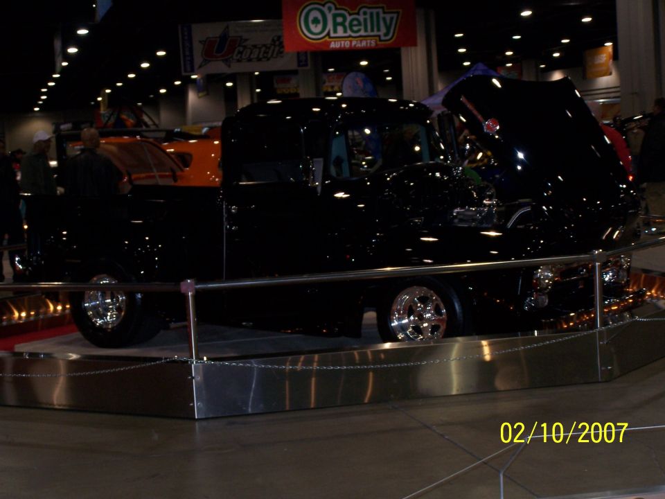 black pickup truck on display, hood up, chrome wheels, indoor event