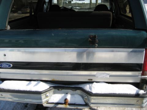 1994 Ford Bronco - The rear of a Ford Bronco is shown with a Ford emblem and a tow hitch. Snow covers the bumper.