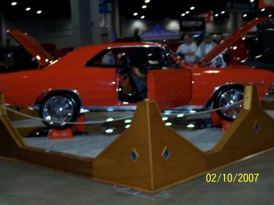 Orange coupe with doors and hood open, chrome wheels, on display