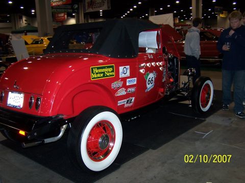 1979 Ford F-150 - A red hot rod is displayed indoors with various sponsor decals on its side.