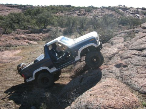 1986 Ford Bronco - A blue and white Ford Bronco navigates a challenging rocky trail during an off-road event.