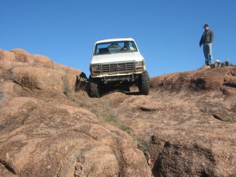 1986 Ford Bronco - White Ford Bronco navigating a steep, rocky incline under a clear blue sky.