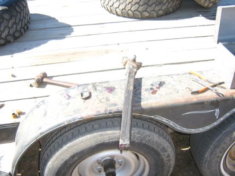 1986 Ford Bronco - A close-up view of a trailer's axle and wheel assembly, showing tools and a damaged spindle.