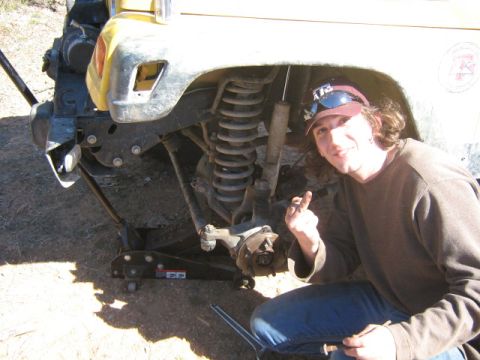 1986 Ford Bronco - A person poses by the front suspension of a yellow SUV, which is supported by jacks.