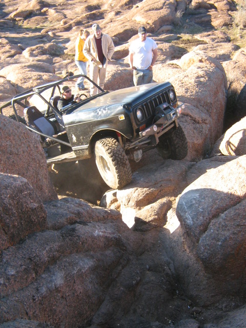 1986 Ford Bronco - Off-road vehicle navigating a rocky terrain with spectators observing.