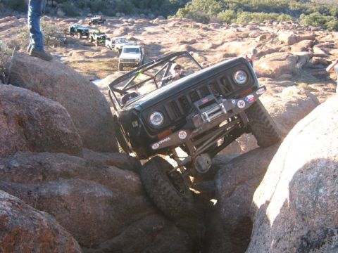 1986 Ford Bronco - Several off-road vehicles navigate a challenging rocky terrain, with one vehicle prominently climbing over large boulders.