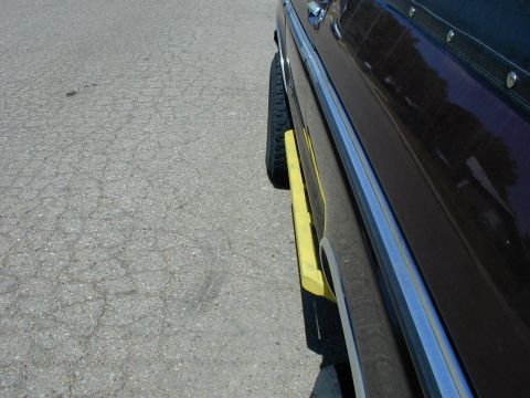 1979 Ford Bronco - Down-the-side detail of a dark maroon truck on cracked asphalt, showing polished chrome bodyside molding and rocker trim with a yellow-pain…