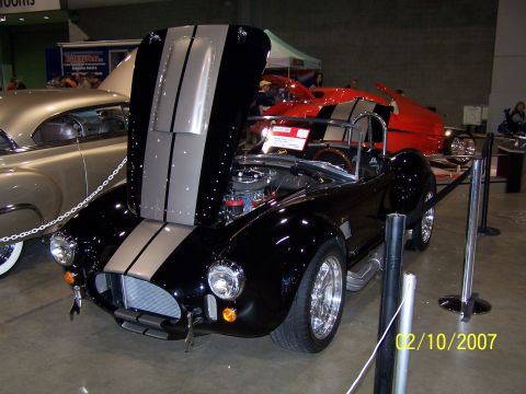 1979 Ford F-150 - A black convertible with silver racing stripes is displayed with its hood open at a car show, with other vehicles visible in the background.