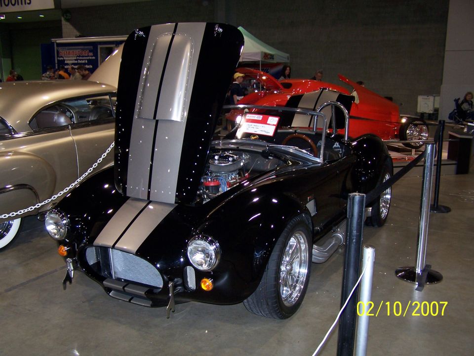 Black convertible with silver racing stripes, hood open, at car show