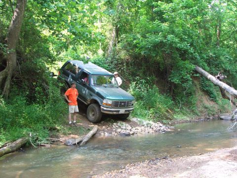 1996 Ford Bronco - A green Ford Bronco navigates a wooded area with a stream crossing.