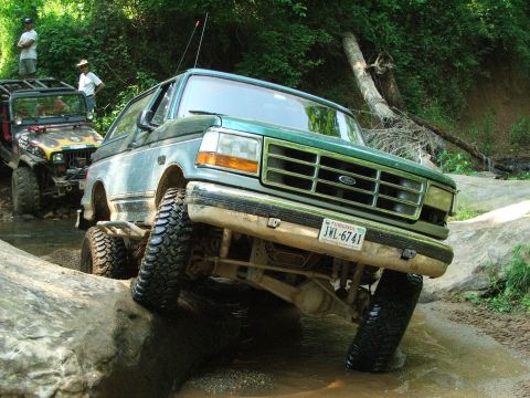 1996 Ford Bronco - A green 1996 Ford Bronco tackles an off-road obstacle course, with another vehicle visible in the background.