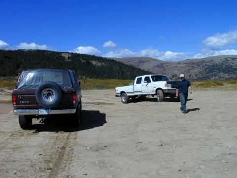 1979 Ford Bronco - Rear view of a maroon Ford full-size Bronco with a black soft top and swing-away spare tire carrier parked on a high-country dirt clearing,…