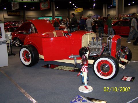 1979 Ford F-150 - A custom red hot rod is displayed indoors with its hood open, revealing a powerful V8 engine.