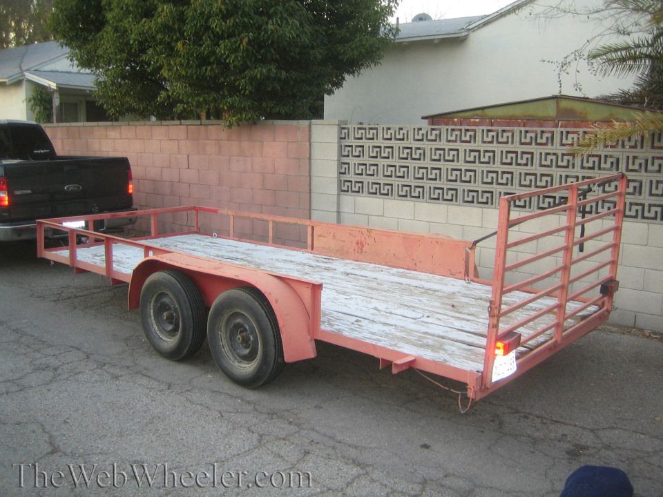 Red utility trailer towed by black pickup truck, parked on asphalt