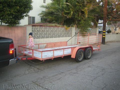 1987 Suzuki Samurai - A young girl stands on a trailer hitched to a pickup truck in a residential area.