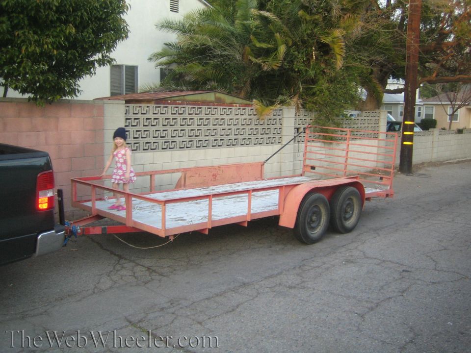 kid standing on a double-axle utility trailer being towed by a dark pickup truck