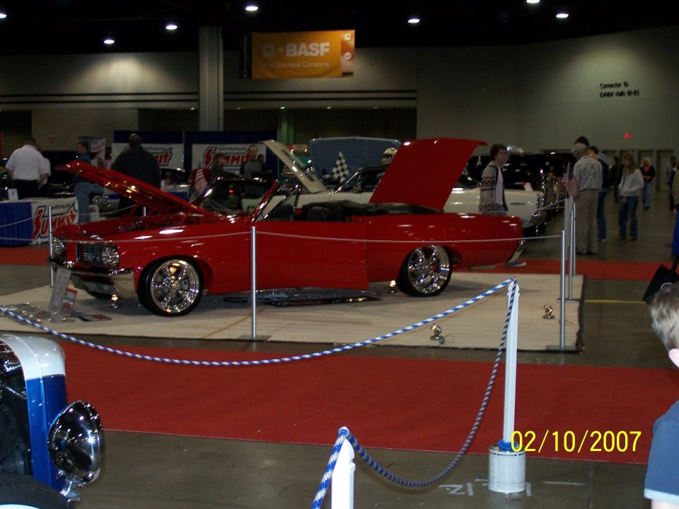 Red convertible with hood and door open, on display at a car show