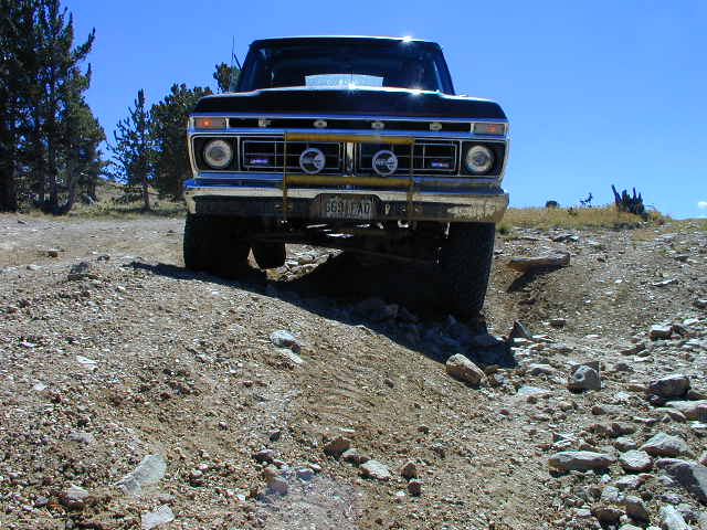 Ground-level front view of lifted dark Ford 4x4 straddling a rocky rutted trail