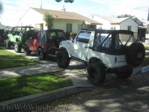 1987 Suzuki Samurai - Three Suzuki Samurai SUVs are parked in a line on a paved driveway in front of houses.