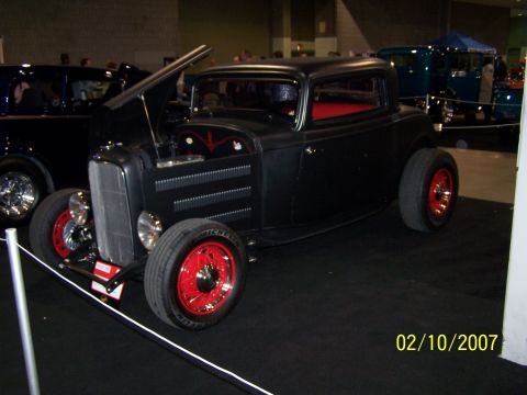 1979 Ford F-150 - A black hot rod coupe with red accents is displayed indoors, with another vehicle visible behind it.
