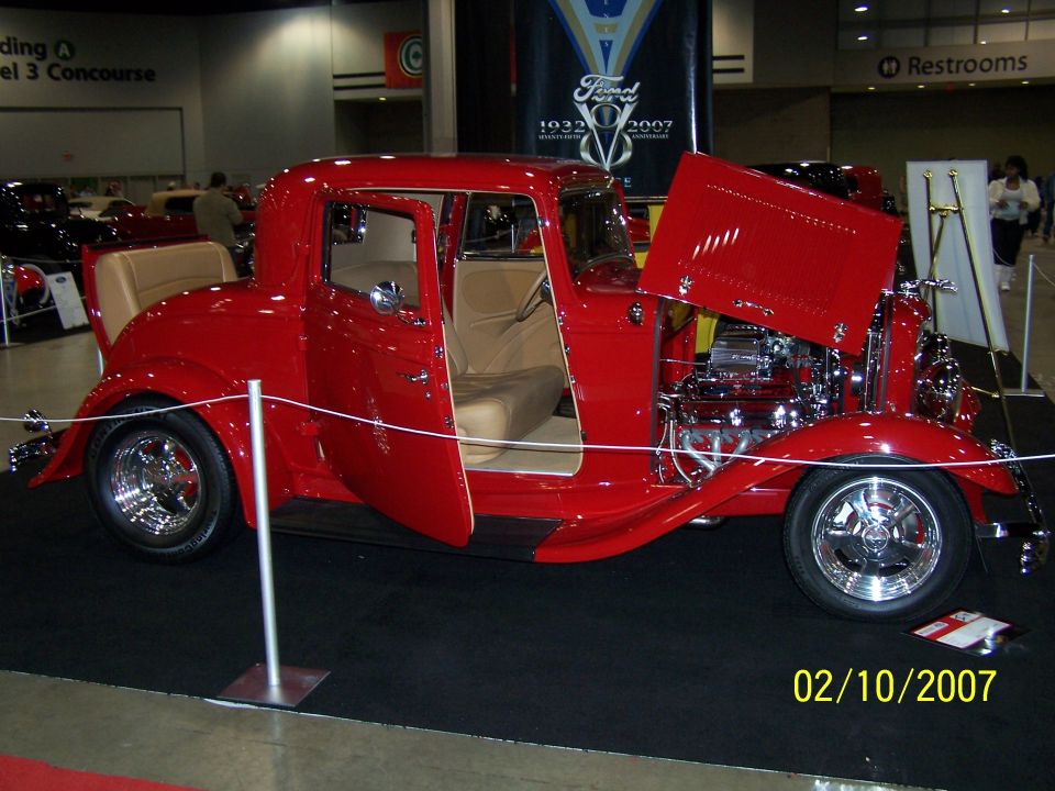Red hot rod coupe with tan interior, doors open, and hood raised showing engine. Date stamp reads 02/10/2007