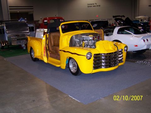 1979 Ford F-150 - A modified yellow pickup truck is displayed indoors with other vehicles in the background.