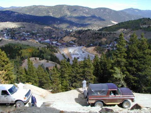 1979 Ford Bronco - Two off-road vehicles navigate a steep, dusty trail overlooking a valley town.