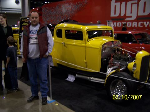 1979 Ford F-150 - A yellow hot rod is displayed indoors with a man standing beside it.