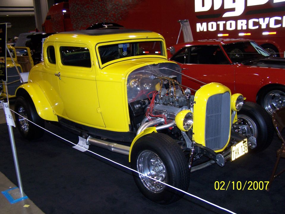 Yellow hot rod coupe with exposed engine and custom grille. Red car behind it