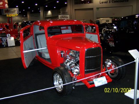 1979 Ford F-150 - A bright red hot rod is displayed with its doors open, revealing a custom interior and a powerful engine. The vehicle is part of a show, as…