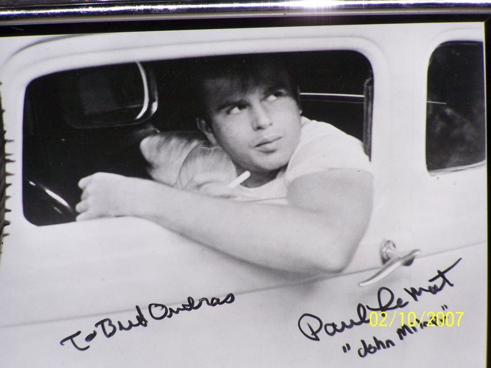 Black and white photo of a man leaning out of a car window, with signatures on the door