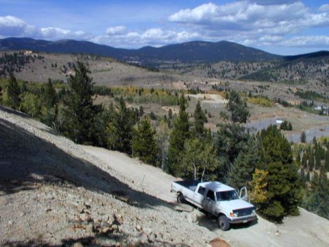 1979 Ford Bronco - A white pickup truck navigates a dirt road with a scenic mountain landscape in the background.