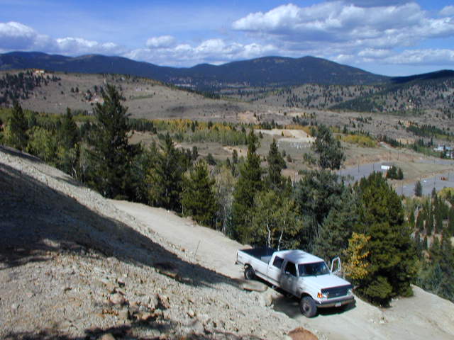 White pickup truck with crew cab on a dirt road in a hilly, wooded area