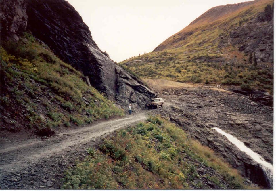 off-road vehicle driving on a narrow dirt road next to a steep mountain slope