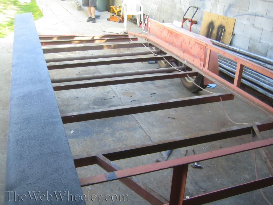 Trailer frame with metal beams and a single wheel visible
