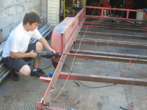 1987 Suzuki Samurai - A man uses a reciprocating saw to cut into the frame of a red trailer.