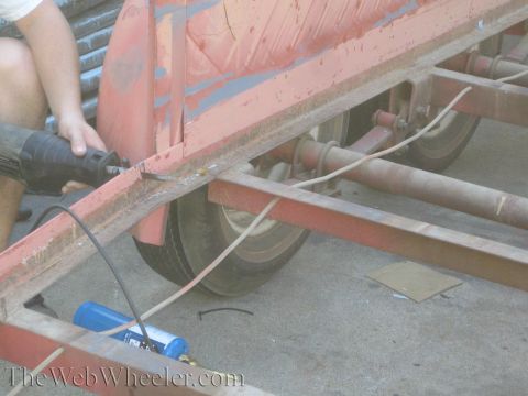 1987 Suzuki Samurai - A person uses a reciprocating saw on the frame of a red trailer, with a propane tank nearby.