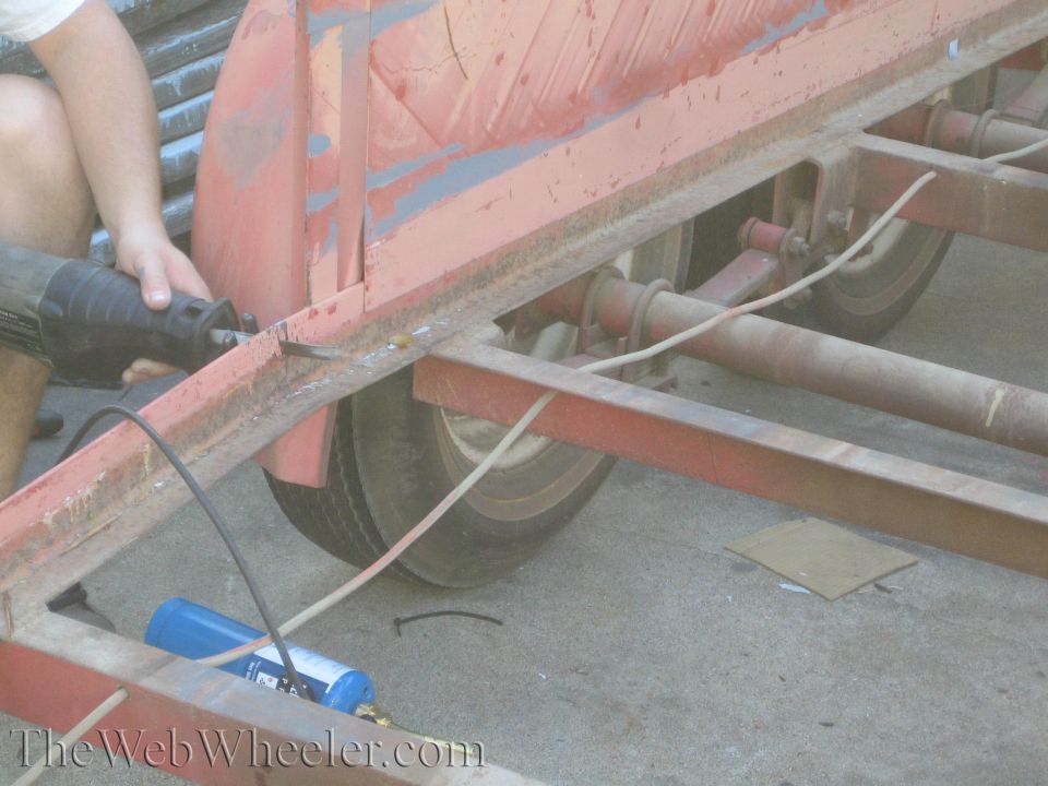 Red trailer frame with a reciprocating saw cutting metal, blue propane tank visible